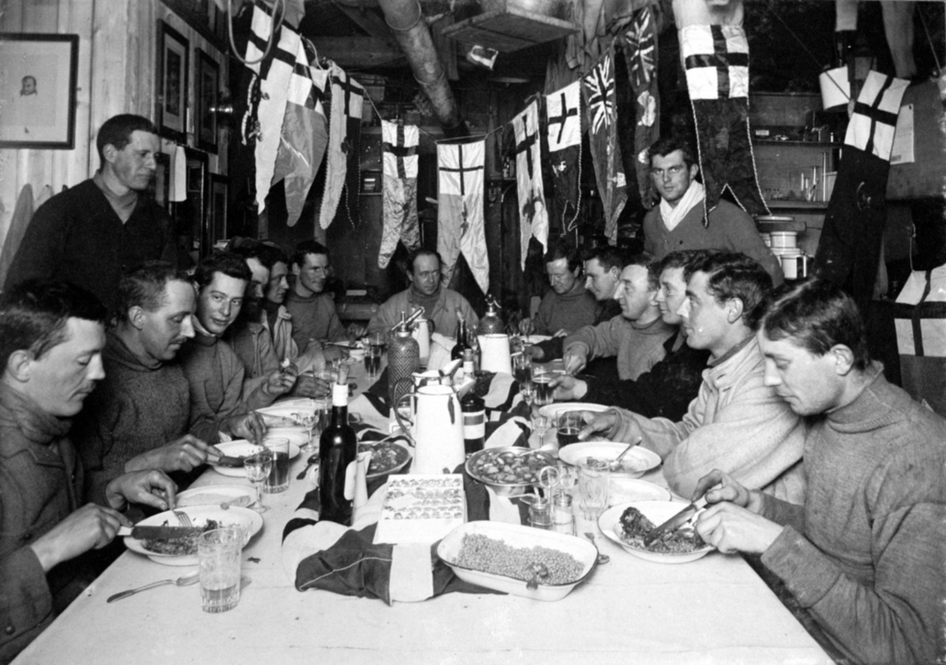 Captain Scott's birthday dinner, 6 June 1911. Left to right: Atkinson, Oates (standing), Meares, Cherry-Garrard, Taylor, Nelson, Evans, Scott, Wilson, Simpson, Bowers, Gran (standing), Wright, Debenham and Day.