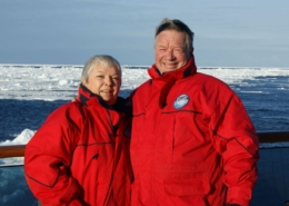A man and woman standing against the rail of a ship with ice floating in the background.
