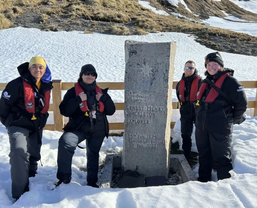 Four people standing beside the tombstone of Ernest Shackleton.