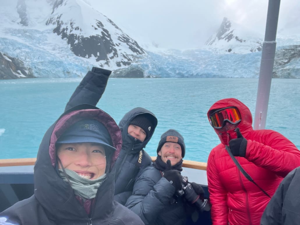 A selfie photo of four people wearing cold-climate clothing in front of a glacier.