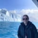 A woman standing on the balcony of a boat, with a large iceberg in the background.