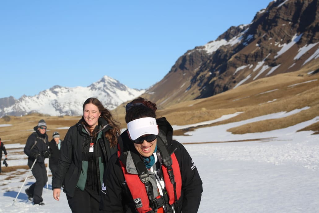 Two women laughing with large mountains in the background.