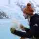 A man holding a sound recording device, directing it towards a glacier.