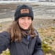 A young woman taking a selfie in front of a penguin colony.