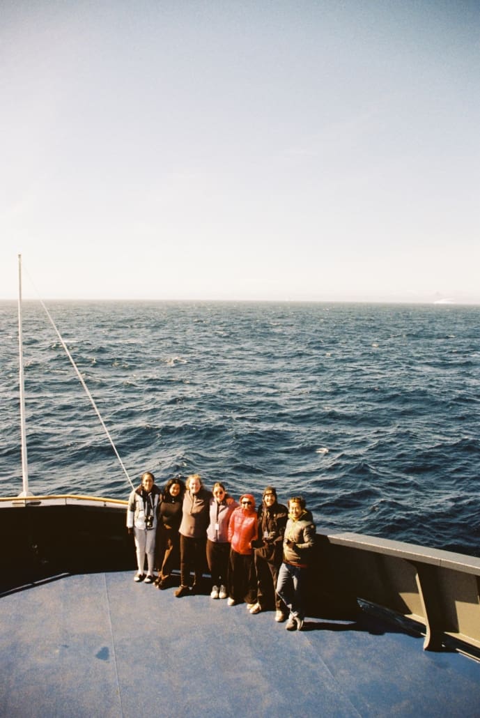 Poeple on the bow of a boat with ocean behind them.