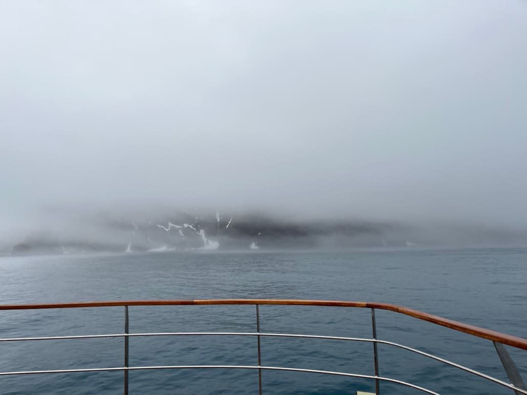 A view of ocean and land, obscured by fog, from the deck of a boat.