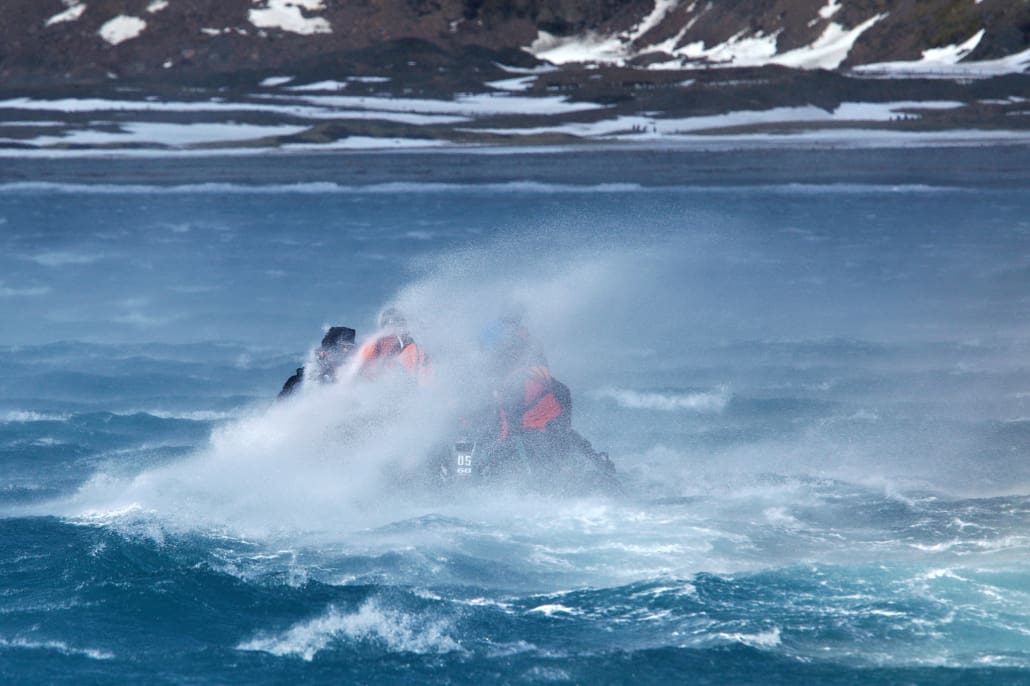 Strong wind blows ocean spray over people in a small boat.